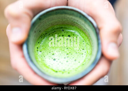 Dessus plat macro closeup de l'homme personne mains tenant un plateau tasse bokeh background en verre vert matcha potable jardin au printemps ou automne Banque D'Images