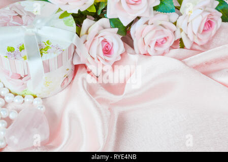 Des roses rose, boîte cadeau ronde et un collier de perles sur un tissu de soie, rose de la composition avec copy-space Banque D'Images