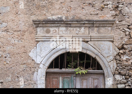 Ornate stone image de la porte d'une maison abandonnée avec des murs en pierre. Partie d'un sol en bois porte fermée. Auvent avec des feuilles d'une plante sauvage. Rue de ret Banque D'Images