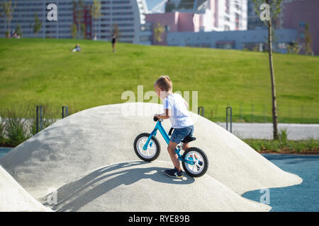 Un petit garçon jouit d'un équilibre vélo sur collines artificielles sur une aire de jeux dans un parc sur une journée ensoleillée d'été. Banque D'Images