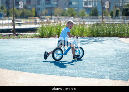 Un petit garçon jouit d'un équilibre à vélo sur une aire de jeux dans un parc sur une journée ensoleillée d'été. Banque D'Images