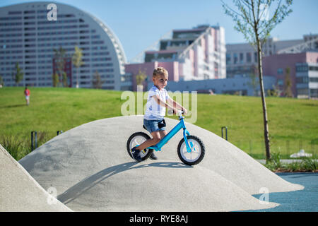 Un petit garçon jouit d'un équilibre vélo sur collines artificielles sur une aire de jeux dans un parc sur une journée ensoleillée d'été. Banque D'Images