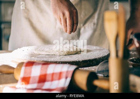 L'homme et de pétrissage de pâte à pizza maison de cuisson dans la cuisine. Gros plan sur les mains du boulanger la préparation du pain. La cuisson et la préparation des aliments à la maison. Banque D'Images