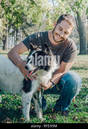 L'homme avec son chien jouant dans le parc en plein air. Jeune propriétaire hugs son animal dans la nature. Banque D'Images