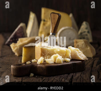 Morceau de fromage Parmesan sur la planche de bois. Assortiment de fromages différents à l'arrière-plan. Banque D'Images