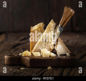 Morceau de fromage Parmesan et de couteau sur la planche de bois. Fond sombre. Banque D'Images