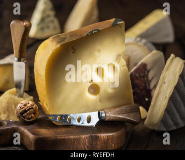Morceau de fromage Maasdam du lait de vache sur planche de bois. Gamme de fromages à l'arrière-plan. Banque D'Images