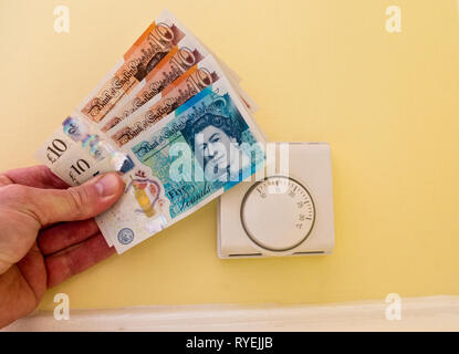 Honeywell Thermostat Chauffage central avec Man's Hand Holding Livre Sterling Argent Notes concernant les coûts de chauffage, UK Banque D'Images