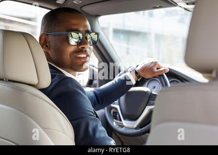 Jeune homme à lunettes pilote assis à l'intérieur voiture conduire maintenant le volant à la caméra arrière siège arrière heureux view Banque D'Images
