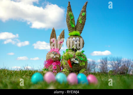 La figure de paille Bunnys avec les oeufs de Pâques colorés en vert grassand Pâques Printemps ciel bleu et l'arrière-plan flou. Banque D'Images