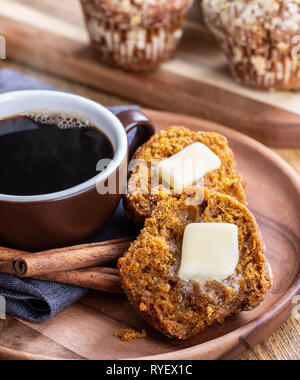 Muffin potiron coupé en deux avec la fonte du beurre et une tasse fumante de café sur une plaque de bois Banque D'Images