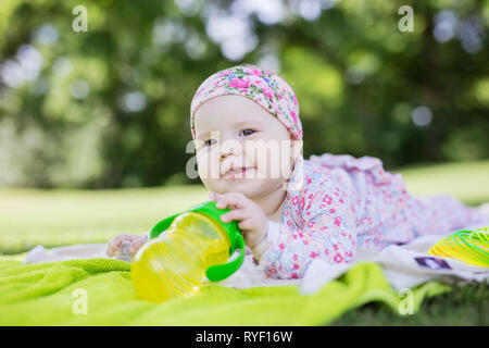 Cheerful baby girl avec une bouteille d'eau couché dans parc d'été Banque D'Images