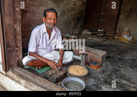 L'homme, l'attente pour les clients, assis en tailleur dans un magasin de la porte avec ses outils de travail en face de lui. Banque D'Images
