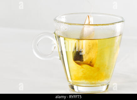 Libre d'un sachet de thé dans une tasse en verre plein d'eau avec de beaux effets de couleur jaune dans la transparence de l'eau Banque D'Images