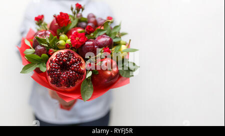 Magnifique bouquet composé de grenade, pommes, raisins, prunes et roses écarlates dans les mains d'une femme sur un fond blanc Banque D'Images