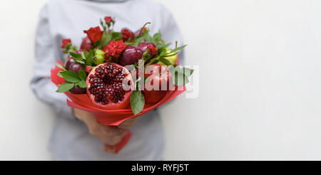 Magnifique bouquet composé de grenade, pommes, raisins, prunes et roses écarlates dans les mains d'une femme sur un fond blanc Banque D'Images