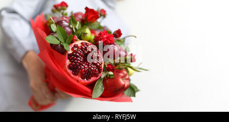 Magnifique bouquet composé de grenade, pommes, raisins, prunes et roses écarlates dans les mains d'une femme sur un fond blanc Banque D'Images