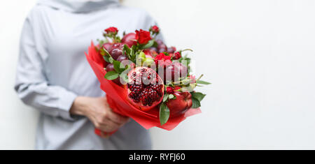 Magnifique bouquet composé de grenade, pommes, raisins, prunes et roses écarlates dans les mains d'une femme sur un fond blanc Banque D'Images