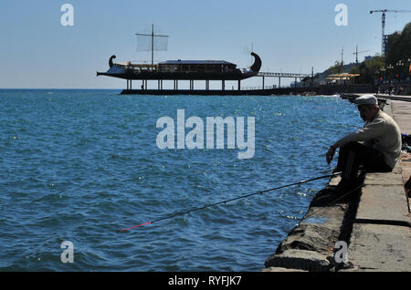 Yalta, Ukraine, mai 2011. Vieil homme à terre Apelʹsyn pêche avec bateau restaurant à l'arrière. Banque D'Images