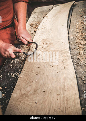 Carpenter à l'époque médiévale vêtements en coton avec un Drawknife ou le dessin d'un couteau ou d'attirer et de rasage rasoir couteau sont des outils à ciseler sur planche de bois Banque D'Images