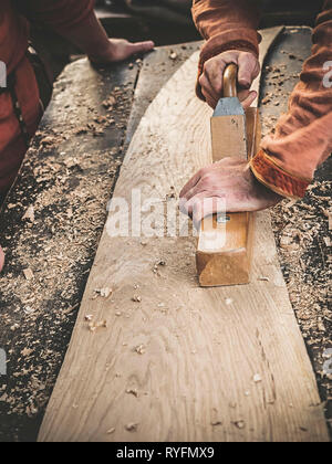 Carpenter à l'époque médiévale vêtements coton Travailler avec un bois en avion. L'homme s'accroche manuellement une planche en bois avec un avion. Construction d'une écorce de bois Banque D'Images