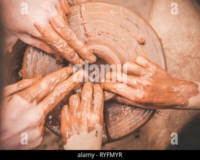 Un carftman poterie enseignement directeurs les mains d'un enfant part, montrant la façon de lancer un pot en argile sur une roue de potier. L'enseignant et l'apprenant concept. Vue d'en haut Banque D'Images