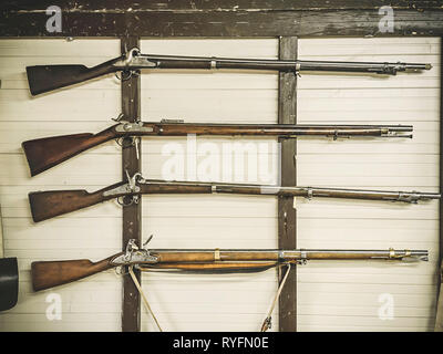 Ancien service rifles de la fiole de poudre militaire accroché sur la paroi en bois. Le fusil sur un mur blanc Banque D'Images