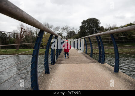 Deux ans en veste rouge et bobble hat sur un pont en bois à la recherche sur le côté au lac ci-dessous Banque D'Images