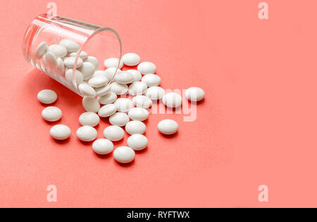 Pilules blanches sur fond rose. Pilules blanches sur le flacon en verre sur fond rose. Banque D'Images