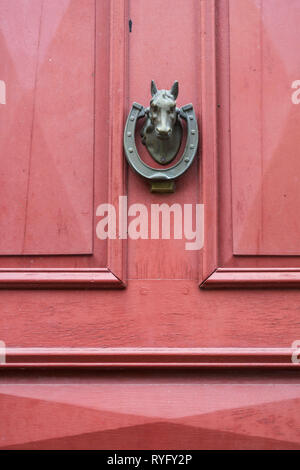 Heurtoir en forme de tête de cheval et fer à cheval sur une porte rouge Banque D'Images