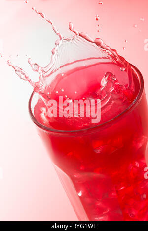 Close up d'un splash sur un verre de jus de fraises sur fond rouge Banque D'Images