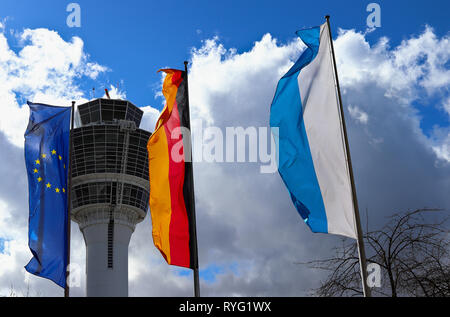 L'AÉROPORT DE MUNICH, Bavière, Allemagne - Mars 13, 2019 : L'UNION EUROPÉENNE drapeau, pavillon de l'Allemagne et la Bavière drapeau d'Etat. Dans l'arrière-plan une tour de contrôle de la circulation aérienne. Banque D'Images