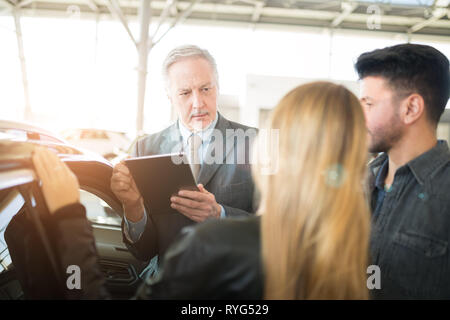 Jeune famille heureuse de parler au vendeur et le choix de leur nouvelle voiture dans un showroom. Effet lens flare Banque D'Images