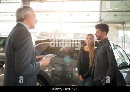 Jeune famille heureuse de parler au vendeur et le choix de leur nouvelle voiture dans un showroom. Effet lens flare Banque D'Images