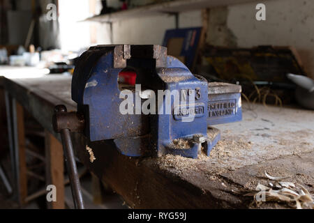 Honiton, Devon, Engalnd, mars, 2, 2019 : un gros plan d'un bleu vif de travail utilisé sur un plan de travail en bois vice dans un atelier couvert de poussière de coupe de bois Banque D'Images