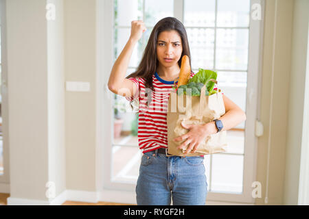 Jeune femme tenant un sac en papier plein d'épicerie contrarié et frustré de crier avec colère, fou et hurlant de main levée, la colère concept Banque D'Images