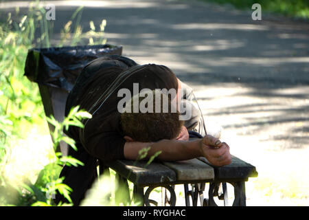 Drunk man sleeping in park sur banc en bois Banque D'Images