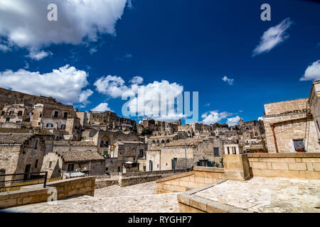 Paysage d'été vue sur la rue de la magnifique vieille ville de la Sassi avec white puffy clouds moving sur le ciel bleu italien. Matera, Basilicate, il Banque D'Images