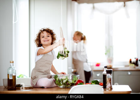 Un portrait de petite fille avec grand-mère dans une cuisine à la maison, préparer une salade de légumes. Banque D'Images