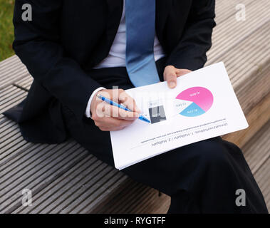 L'homme d'affaires examine les graphiques assis dehors sur un banc Banque D'Images