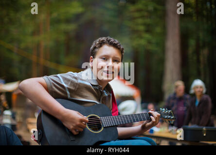 Portrait of boy smiling comme il joue une guitare acoustique dans un emplacement en extérieur. Banque D'Images