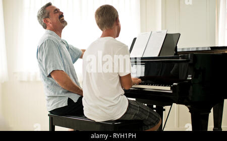 L'adulte homme d'enseigner son fils adolescent à jouer du piano. Banque D'Images