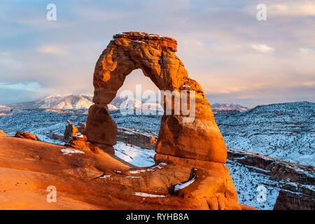 Delicate Arch iconique éclairé avec heure d'or lumineux lumière avec Montagnes La Sal derrière après une tempête de neige en février 2019 Arches National Park, Moab, Banque D'Images