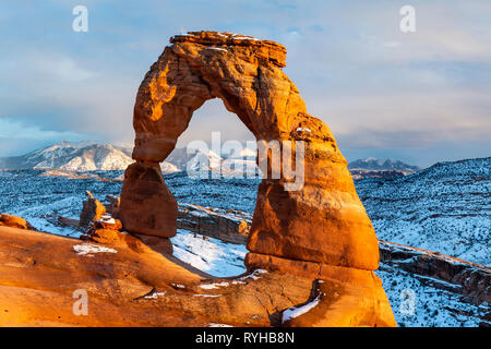 Delicate Arch iconique éclairé avec heure d'or lumineux lumière avec Montagnes La Sal derrière après une tempête de neige en février 2019 Arches National Park, Moab, Banque D'Images