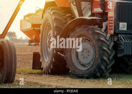 Vieux tracteur agricole rouge avec remorque sur la saleté route de campagne au printemps après-midi Banque D'Images