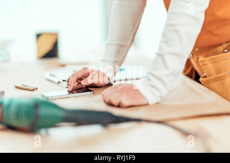 Female carpenter est l'utilisation de téléphone mobile pour la messagerie texte, la saisie de sms sur l'écran tactile du smartphone, selective focus Banque D'Images