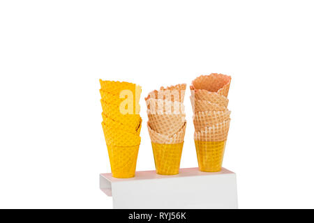 Des cornets de crème glacée faite de gaufrettes au four en forme de cônes avec différentes nuances de couleurs dans des gobelets en plastique sur un support isolé sur un fond blanc. Banque D'Images