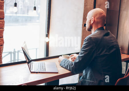 Penser avec succès adultes attrayant barbu chauve man with laptop in cafe Banque D'Images