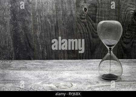 Hourglass avec grains de sable noir sur fond vintage en bois. Banque D'Images
