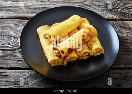 Close-up de rouleaux de crêpes au fromage à la crème garniture sur une plaque noire sur une vieille table en bois. Vue du dessus horizontale Banque D'Images